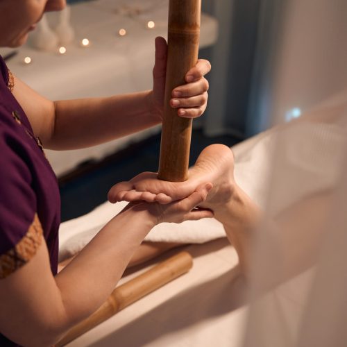 Cropped photo of masseuse pressing with bamboo cane end on client foot reflex point