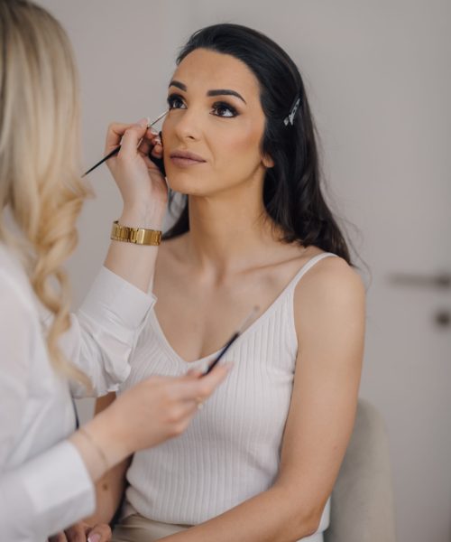 Professional makeup artist carefully applying eyeshadow on a beautiful model's face, preparing her for a photoshoot or special event